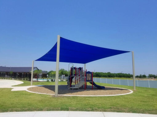 Blue shade sail over a playground next to a lake