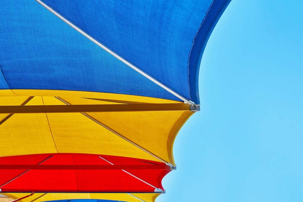 Brightly colored outdoor sun shade structures in red, yellow, and blue, designed to block UV rays and add visual appeal to open parking or public spaces.