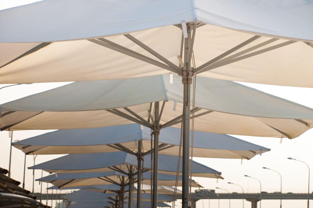 Row of waterproof commercial shade umbrellas installed in an exterior parking area, providing sun and rain protection. 