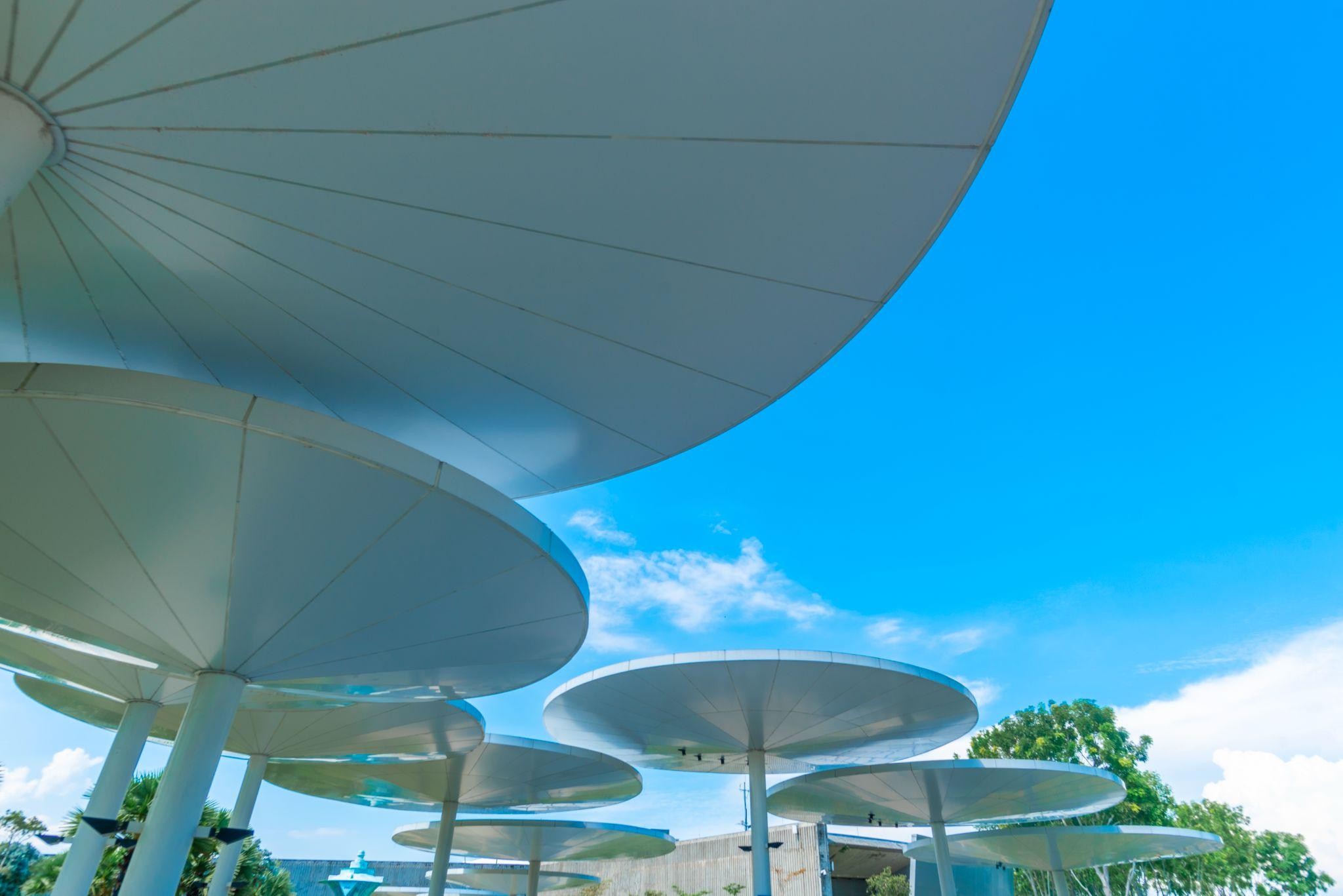 Modern waterproof exterior shade structures with circular canopies designed for commercial outdoor use under a clear blue sky.