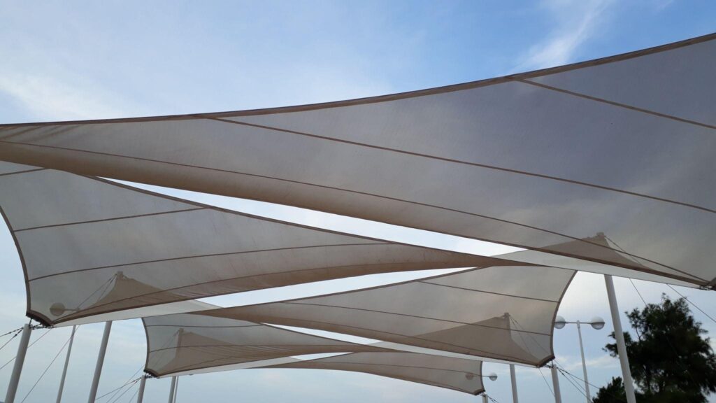 Light beige shade sails stretched across an outdoor area, providing UV protection and sustainable shade with proper tensioning and marine-grade hardware.