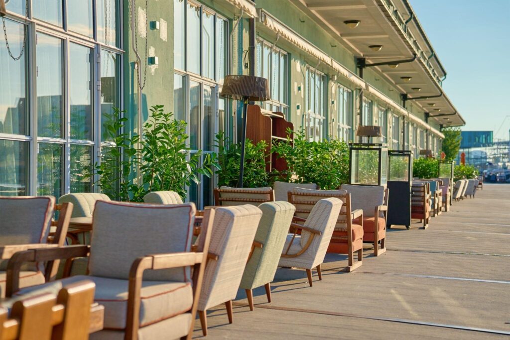 Restaurant patio with retractable awnings providing sun shade for patio dining, empty morning seating along a waterfront walkway.