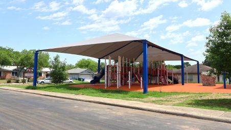Connected outdoor shade structures covering a playground with slides and climbing equipment