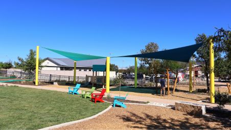 Triangular outdoor shade structure installed over picnic tables at a community playground
