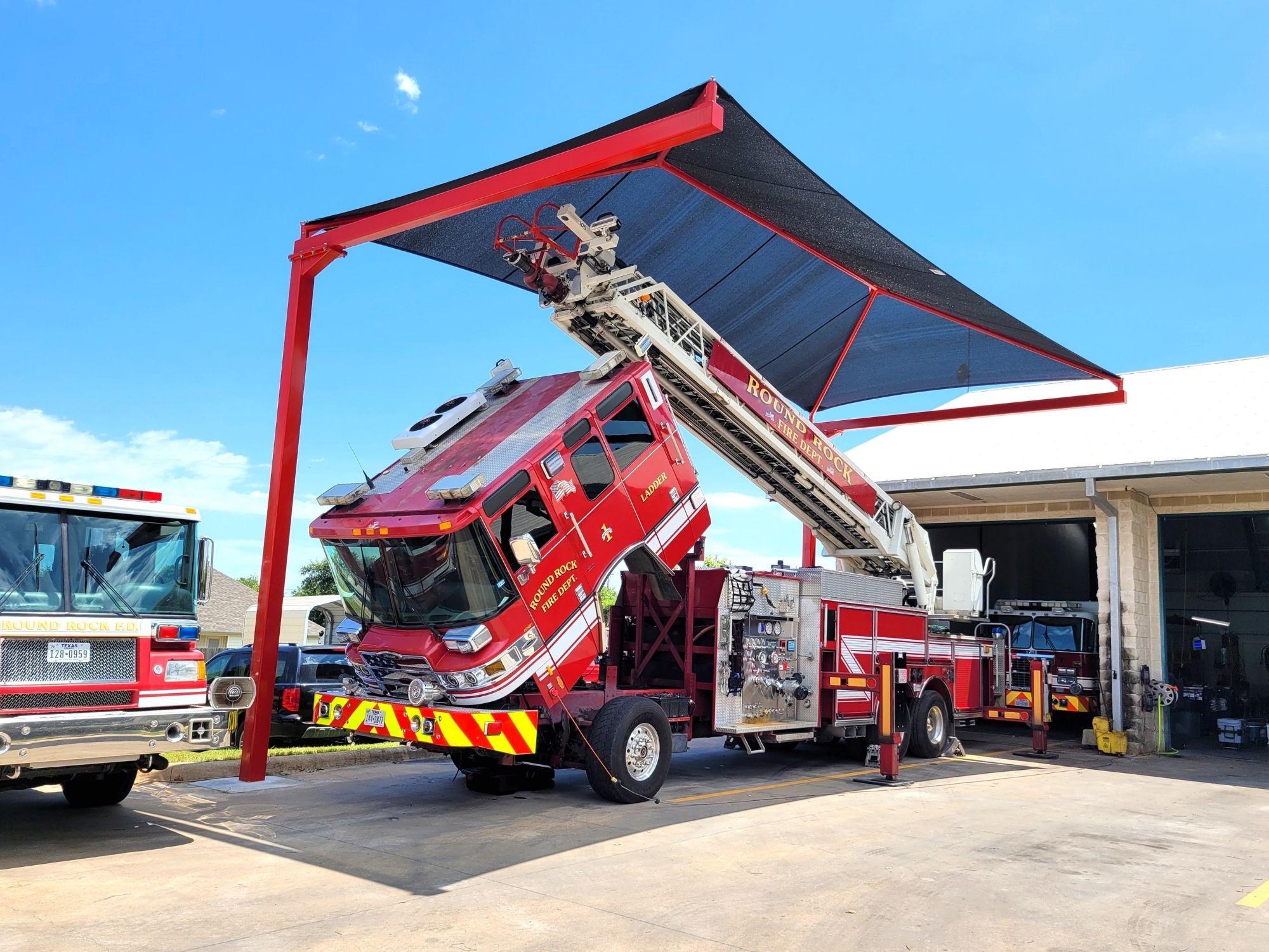 Fabric carport shade structure covering vehicles in outdoor parking lot.