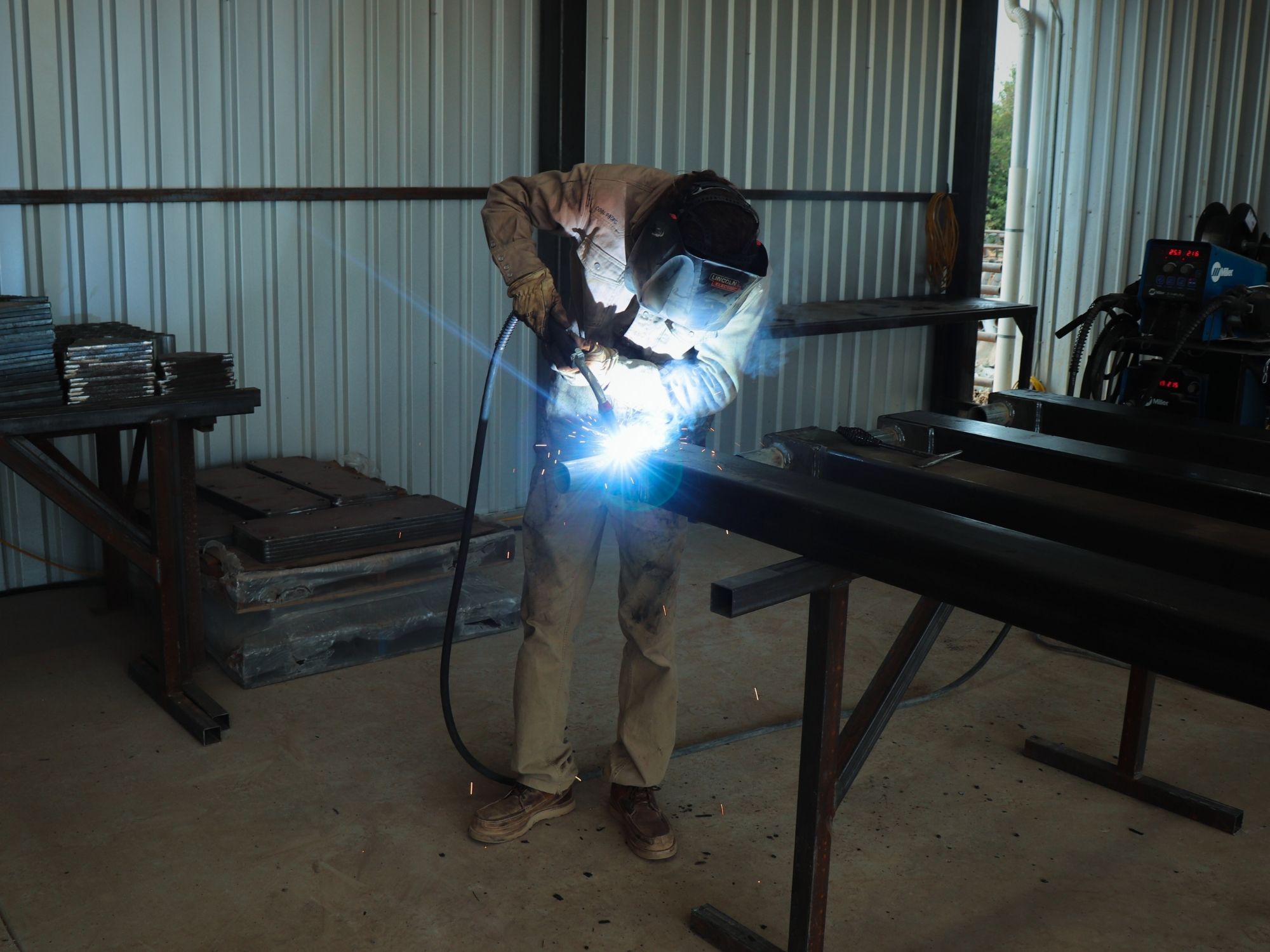Technician welding metal frame during shade structure fabrication.